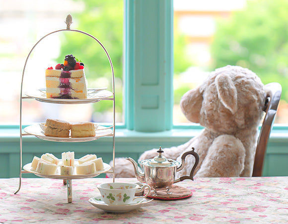 窓際の席にすわるくまのぬいぐるみとアフターヌーンティーセット